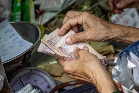 Close up detail of an old woman's hands as she counts out 1000 Baht Thai notes while buying goods