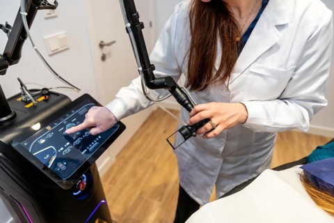 Aesthetician in a white lab coat controlling a professional laser hair removal machine with a