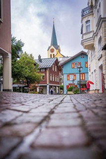 Urban line of sight with cobblestones, towering church tower and colorful buildings, Oberstaufen,