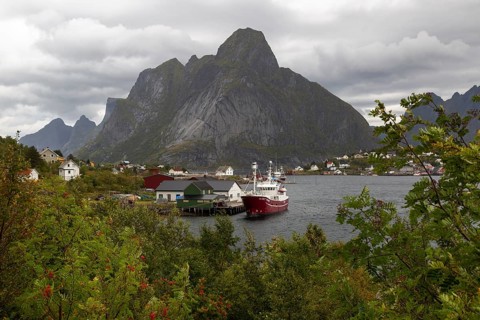 Red fishing boat on pier in Reine harbour in front of the majestic Olstinden mountain under cloudy