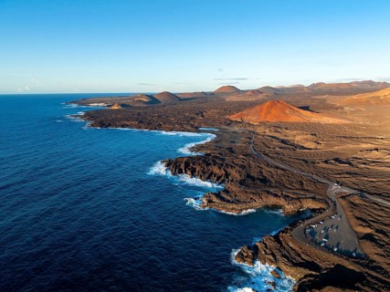 Coast with lava fields, volcanic landscape near Los Hervideros with red volcano Montaña Bermeja, in