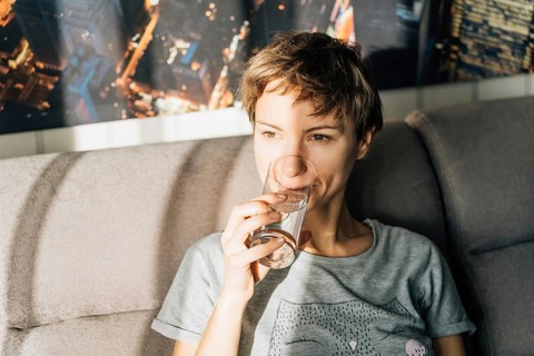 Portrait of a short-haired young woman drinking water from a glass, Woman sitting on a couch,