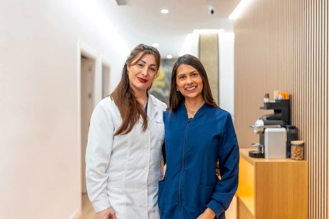 Two smiling female doctors, one wearing a white lab coat and the other a blue scrub, posing in a