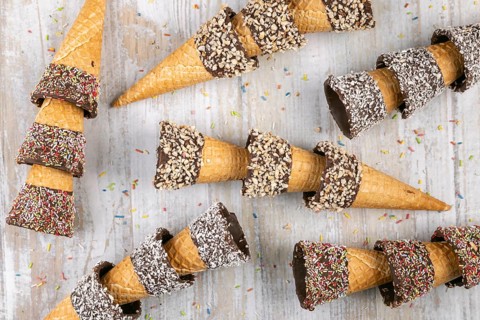 Ice cream cones with colorful sprinkles, chocolate and nuts on wooden background