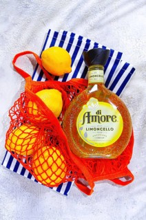 A bottle of limoncello is placed on a blue and white striped cloth. Fresh lemons are next to the