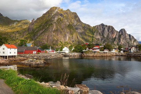 Idyllic bay in a fishing village in front of a huge, steep rock face with traditional Scandinavian