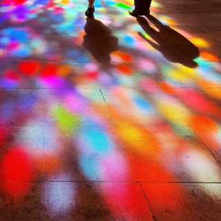 Shadows of two people and colorful spots of light on the floor through the stained glass windows by