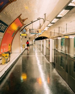 Underground platform of a subway station with a vaulted, white-tiled ceiling, large advertising