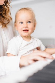 Close-up of a child with curious expression looking up while sitting at a piano