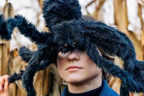 A huge black shaggy toy spider on a woman's head closes her eyes. Halloween Party Costumes and