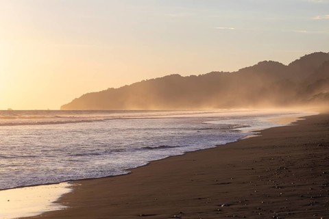 The low sun's golden light illuminates the ocean spray on Carate Beach, with views of Corcovado NP