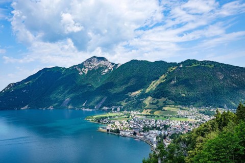 Urban coastal community at the foot of a mountain with houses, blue water and wooded hills under a