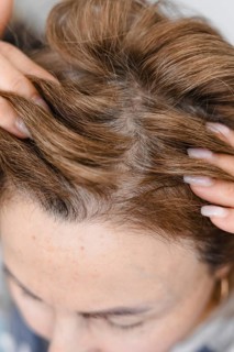 Mature middle-aged caucasian woman touching her gray, silver roots hair close-up on gray tiles