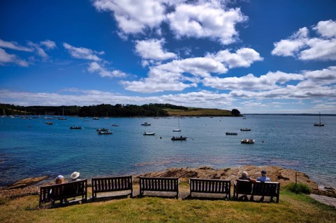 People sitting on a bench in a park and looking at boats in the harbor, sea, clouds, St Mawes,