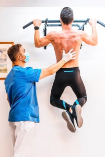 Physiotherapist helping a shirtless patient with a dominated one. Physiotherapy with protective