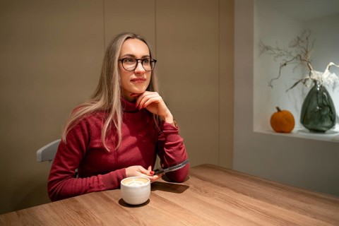 Young woman in glasses with cappuccino in cafe, A woman in a red sweater sits at a wooden table