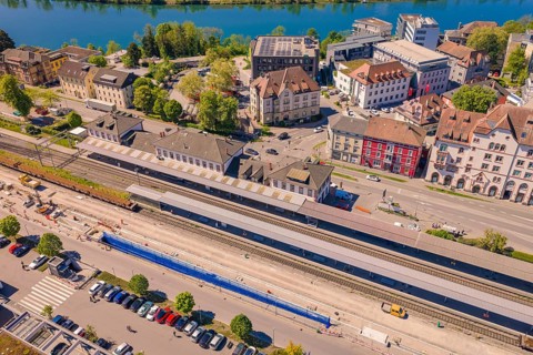 Urban area with railway tracks near a river, surrounded by historic buildings and green landscape