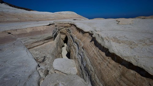 Erosion cracks in dry rock under clear blue sky, white volcanic strata, bizarre white rocks in the