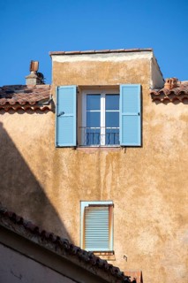 Blue shutters and a small window stand out on a weathered ochre facade beneath terracotta roof
