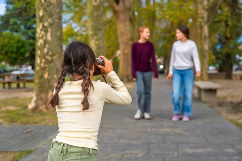 Young girl holding a vintage camera, looking through the viewfinder and capturing casual moments of