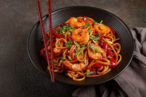 Udon stir-fry shrimp noodles with red bell pepper and green onion, served in a black bowl, with
