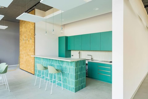 Modern kitchen with green tiles and cabinets and bar stools, illuminated by stylish hanging lamps