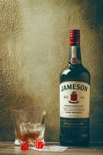 A bottle of Jameson whiskey stands on a wooden table next to a glass filled with whiskey and ice.
