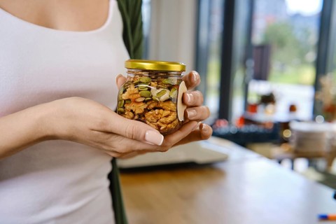 Close-up view of jar filled with honey and mixed nuts and pumpkin seeds in female hands