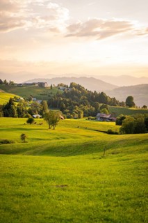 Extensive green meadows and hills with small villages on the horizon in the evening light,
