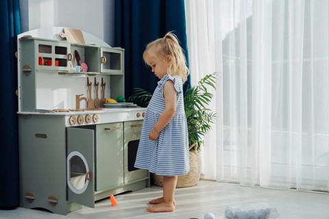 Young child smiles while playing with kitchen toys in well-decorated, light-filled room. The