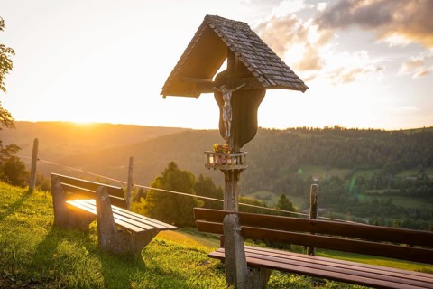 A wooden cross near benches with a view of a beautiful landscape at sunset, Oberstaufen region,