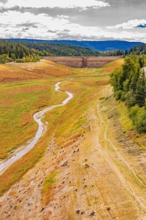 A narrow river flows through a valley with a dam in the background, rehabilitation of the