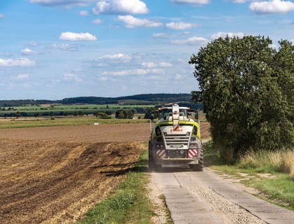 Claas Jaguar 900 series self-propelled forage harvester on a rural path near a harvested field,