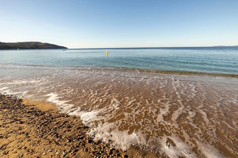 Low beach-level viewpoint over wet sand and sea foam with calm blue water, yellow buoys, distant