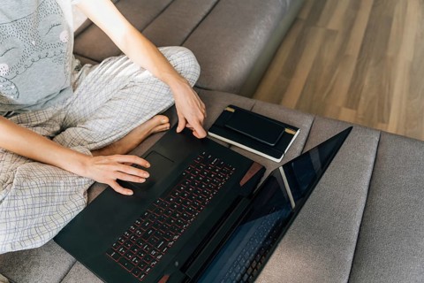 A young woman in pajamas sits on the couch and uses a laptop, Person sitting cross-legged on a