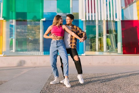 A joyful lesbian couple dances together in an urban setting, sharing laughter and movement. The