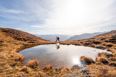 Mountaineer hiking with poles, reflected in a small mountain lake on the Krahberg, mountain