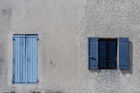 Windows with blue shutters on a gray plaster wall radiate Mediterranean peace, Provence, France