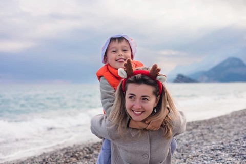 A mother and her young son play on a winter beach. The mother has long blond hair and wears a