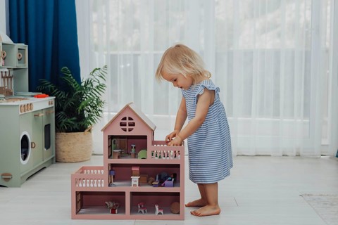 Little girl toddler in striped dress enjoys imaginative play with a doll house in a sunny space