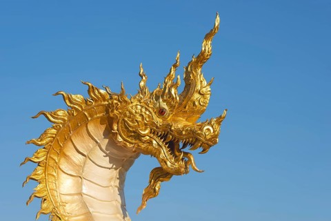 The golden Naga dragon rises against the clear sky of the Khao Kho Mountains. Its flame-like