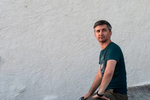 A middle-aged man sits against a white wall in summer clothes, A person is casually sitting