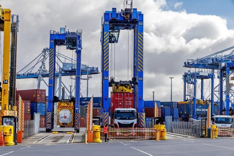 Tall blue straddle carriers straddling a truck with CMA CGM containers at Port of Auckland under
