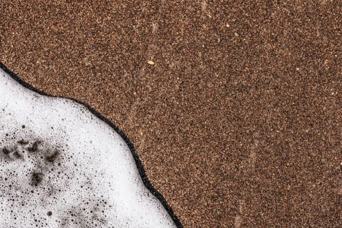Close-up of sandy beach with gentle waves lapping at the shore. The sand is light brown and