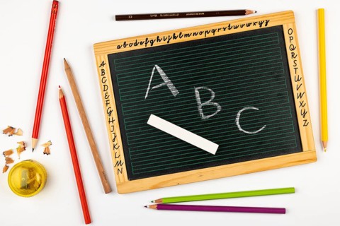 School blackboard with letters surrounded by colored pencils and a sharpener