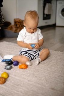 Baby concentrating on a blue toy while seated on a rug