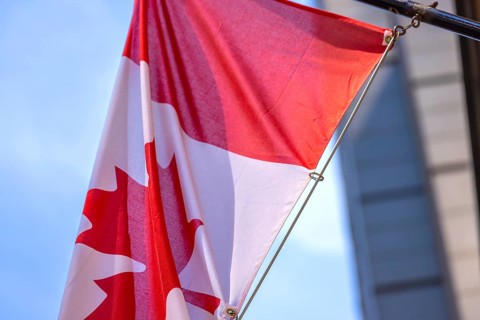 Red and white Canadian flag with a maple leaf waving in the air in downtown Toronto near Ontario