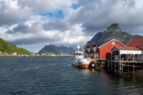 Ship and rorbuer, typical red wooden houses, stilt houses on the banks of Reinefjord, Reine,