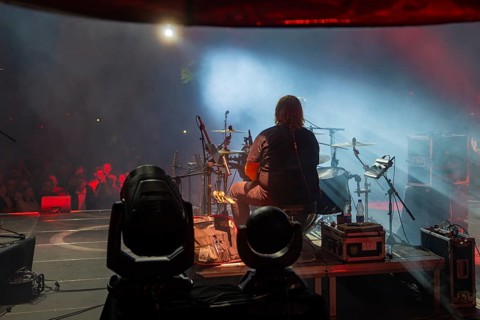 Back view of a musician playing drums on stage, fog effects and audience in the background, Calwer