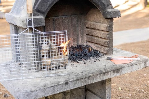 A stone barbecue grill with burning charcoal and flames. A metal grill rack is placed on top. The